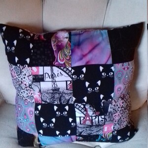 Puede incluir: Una almohada de patchwork con un estampado de gato blanco y negro, un estampado con tem&aacute;tica de Par&iacute;s y un estampado paisley. La almohada est&aacute; hecha de diferentes telas y tiene una variedad de colores, incluyendo negro, blanco, rosa, azul y gris.