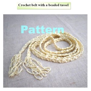 May include: A cream-colored crochet belt featuring a braided cord design and two long tassels at the ends. The tassels are embellished with small white beads. The text "Crochet belt with a beaded tassel" and the word "Pattern" appear in the image.