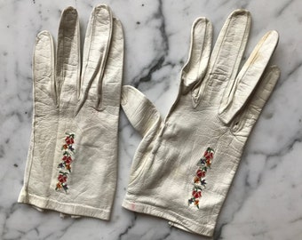 May include: A pair of white leather gloves with embroidered floral designs on the back of each glove.