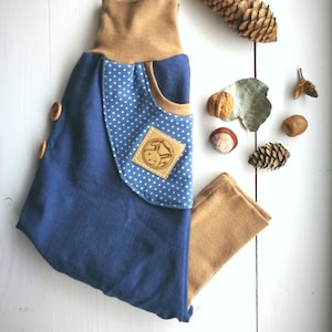 Può includere: Pantaloni per neonati blu e marroni con pois bianchi e una toppa marrone con un logo di coniglio. I pantaloni hanno una cintura a pieghe.