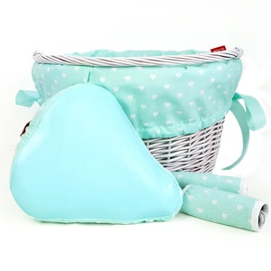 May include: White wicker bicycle basket with a light blue and white heart patterned liner. The basket comes with a light blue padded seat cushion and two matching handlebar grips.