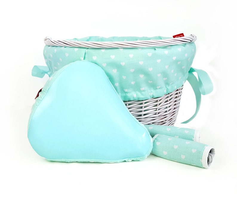 May include: White wicker bicycle basket with a light blue and white heart patterned liner. The basket comes with a light blue padded seat cushion and two matching handlebar grips.
