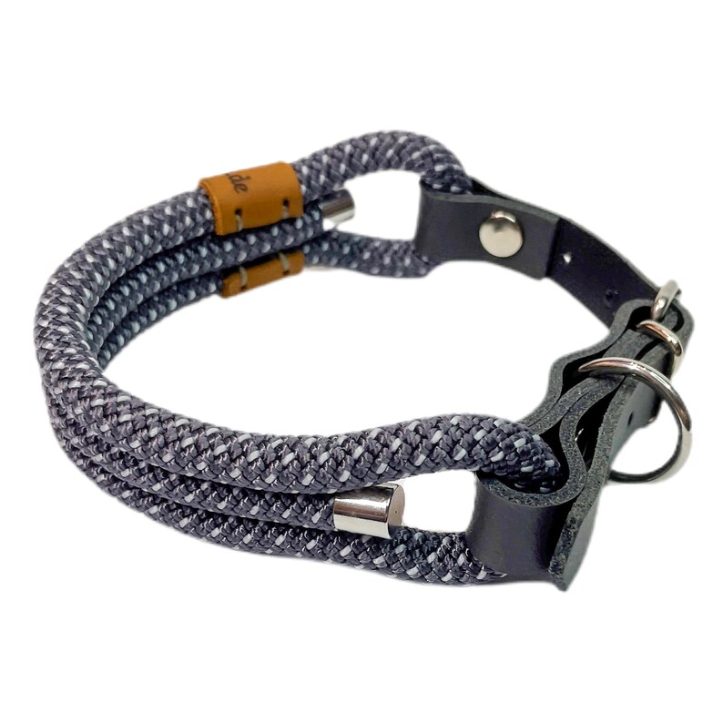 May include: Gray and white rope dog collar with a black leather strap and silver metal hardware. The collar has a buckle closure and a D-ring for attaching a leash.
