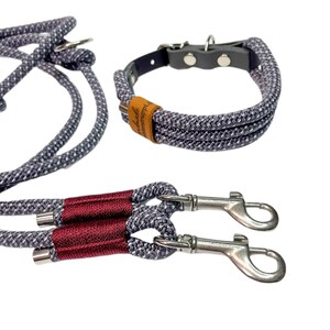 May include: A gray and white rope dog collar and leash set with a red accent on the leash. The collar has a brown leather patch with the text "Handmade with Love" on it. The leash has two silver clips.