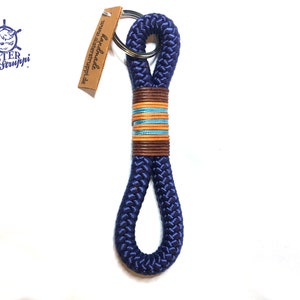 Könnte beinhalten: Ein dunkelblauer Schlüsselband aus Seil mit einem braunen, orangefarbenen und blauen Streifenakzent. Der Schlüsselband hat einen silbernen Schlüsselring und ein braunes Leder-Etikett mit der Aufschrift "handmade" und "www.alsterstruppi.de".
