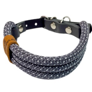 May include: A gray and white rope dog collar with a black leather strap and silver buckle. The collar has a brown leather patch with the text "Happi.de" on it.