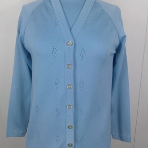May include: A light blue cardigan sweater with a mock neck top underneath. The cardigan has a button-up front and a diamond-shaped pattern.