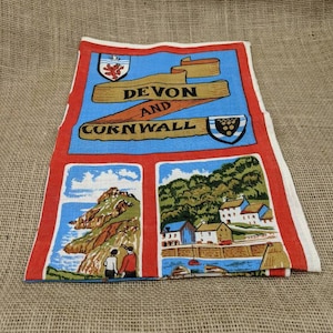 May include: A vintage tea towel featuring a colorful design with the words "Devon and Cornwall" on a blue background. The towel has a red border and includes illustrations of coastal scenes and a couple holding hands.