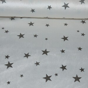 Peut inclure: Tissu satin blanc avec un motif d'étoiles noires. Le tissu est plié en deux, montrant le motif des deux côtés.