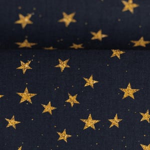 Op de afbeelding: Close-up van een marineblauwe stof met een herhaald patroon van gouden glittersterren. De sterren variëren in grootte en zijn verspreid over het oppervlak, met kleine gouden spikkels die bijdragen aan het hemelse ontwerp.