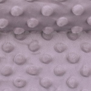 Könnte beinhalten: Nahaufnahme eines weichen, grauen Stoffes mit einem strukturierten, gepunkteten Muster. Der Stoff besteht aus einem plüschigen Material mit kleinen, erhabenen Kreisen.