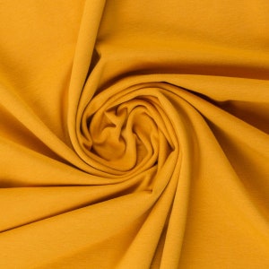 Könnte beinhalten: Nahaufnahme eines weichen, gelben Stoffes mit glatter Textur. Der Stoff ist gefaltet und drapiert und erzeugt ein wirbelndes Muster.