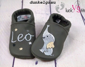 May include: A pair of dark grey leather baby shoes with embroidered stars and the name "Leo" on one shoe and an elephant on the other. The shoes are made by "lucky stitches".