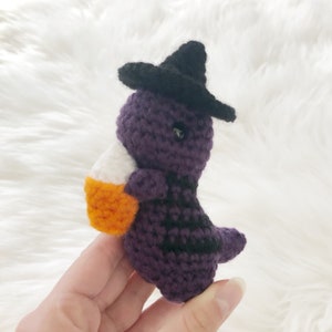 May include: A handmade crochet Halloween decoration featuring a purple witch with a black hat and stripes, holding a candy corn. The whimsical figure is a unique, festive addition to any Halloween decor.