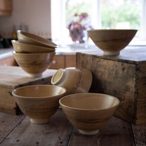 May include: A set of six wooden bowls with a light brown glaze and dark brown streaks. The bowls are stacked and arranged on a wooden surface.