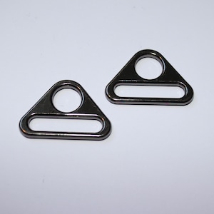 Könnte beinhalten: Zwei silberne dreieckige Metallringe mit einem kleinen Loch oben und einer größeren rechteckigen Öffnung in der Mitte.