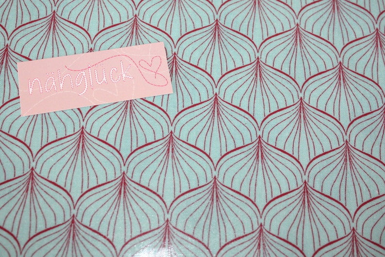 Puede incluir: Una tela azul claro con un patr&oacute;n repetitivo de formas de hojas granates. Una tarjeta rosa con la palabra "n&auml;hgl&uuml;ck" y un coraz&oacute;n est&aacute; colocada encima de la tela.