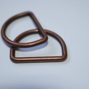 Könnte beinhalten: Zwei antike kupferfarbene D-Ringe aus Metall. Die Ringe sind übereinander gestapelt.