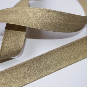 Könnte beinhalten: Ein goldfarbenes Band mit einem dezenten Schimmer. Das Band ist flach und hat eine glatte Textur.