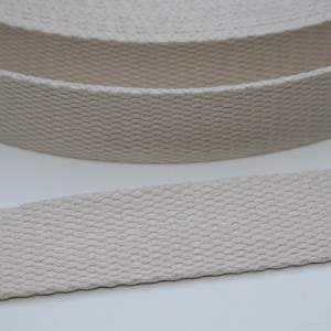 Op de afbeelding: Een close-up van een beige katoenen band. De band is geweven met een textuurpatroon en is opgerold.