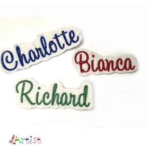 May include: Three embroidered name patches: "Charlotte" in blue, "Bianca" in red, and "Richard" in green. Each name is stitched on a white, cloud-shaped felt patch. The "Home Artist" logo is visible in the bottom left corner.