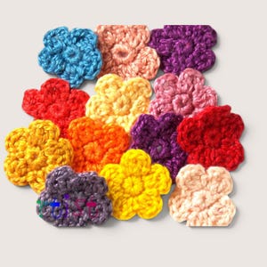 May include: A collection of twelve small, five-petaled crochet flowers in various colors including blue, peach, purple, red, yellow, orange, and pink. Each flower is crafted from yarn with a visible textured stitch pattern and a central knot.