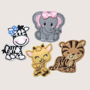May include: Four embroidered fabric patches featuring cartoon animals: a white and black zebra with a blue bow, a gray elephant with a pink bow, a yellow giraffe, and a brown tiger with dark stripes, all with stitched outlines and details.