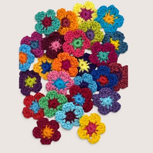 May include: A collection of small, five-petaled crochet flowers in a variety of vibrant colors including yellow, orange, red, pink, purple, blue, and green. Each flower features a contrasting center color, creating a diverse assortment of handmade textile embellishments.