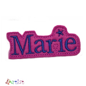 May include: Pink felt name tag with the name "Marie" embroidered in blue thread. A small blue star is above the name.