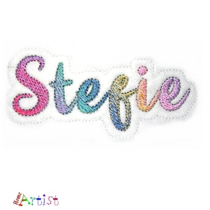 May include: Rainbow embroidered name "Stefanie" in a cursive font. The name is stitched on a white fabric background.