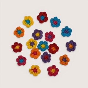 May include: A collection of seventeen small, five-petaled crochet flowers in various vibrant colors including red, yellow, orange, blue, and purple. Each flower features a contrasting colored center, arranged in a circular pattern on a plain background.
