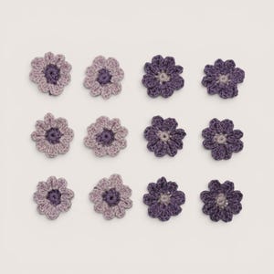 May include: A collection of twelve crocheted flower appliques arranged in a grid. The left two columns feature light lavender and mauve petals with dark purple centers, while the right two columns feature deep purple petals with light gray centers.