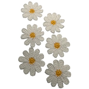 May include: A collection of six individual crochet daisy appliques. Each flower features white petals arranged in a circular pattern around a central yellow core. The crochet work displays a textured, stitched surface with distinct petal shapes.