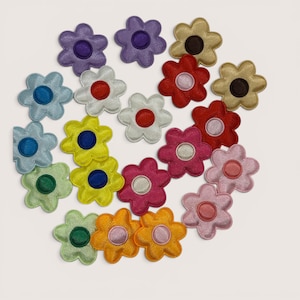 Könnte beinhalten: Eine Sammlung von einundzwanzig Stoffblumen-Aufnähern in verschiedenen Farben, darunter Lila, Blau, Gelb, Grün, Weiß, Rot, Pink und Orange. Jeder Aufnäher hat eine sechsblättrige Blumenform mit einem kreisförmigen Zentrum in Kontrastfarbe.