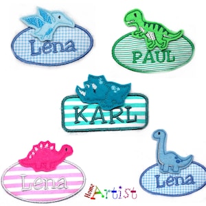 May include: A collection of colorful dinosaur-themed name patches. Each patch features a different dinosaur design, including a pterodactyl, T-Rex, and Triceratops, with names like "Lena", "Paul", and "Karl" embroidered on them. The patches have various background patterns.