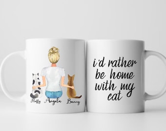 May include: White ceramic mug with a design featuring a woman with blonde hair, two cats, and the text "I'd rather be home with my cat." The cats are a black and white cat and a brown cat. The names "Fluffy", "Angela", and "Bunny" are written below the cats.