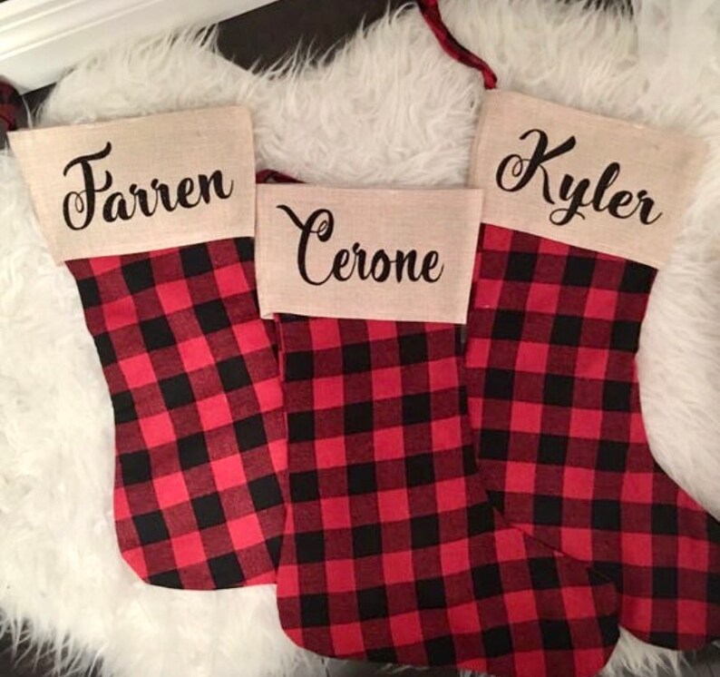 May include: Three Christmas stockings featuring a red and black buffalo plaid pattern. Each stocking has a tan burlap cuff at the top. The names Farren, Cerone, and Kyler are printed in black cursive script on the cuffs of the three stockings.