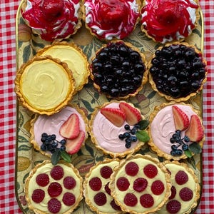 Könnte beinhalten: Ein Tablett mit verschiedenen Mini-Törtchen mit verschiedenen Belägen. Einige Törtchen haben rote Früchte und Schlagsahne, andere Blaubeeren, Erdbeeren und Himbeeren. Die Törtchen liegen auf einem dekorativen Tablett.