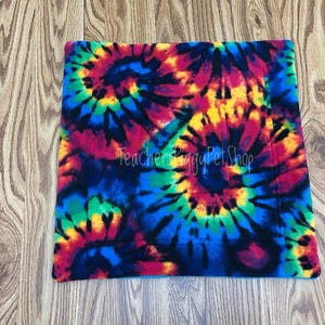 May include: A square, tie-dye pet bed in vibrant colors of red, yellow, blue, and green. The bed features a swirling pattern and the text "Teachers Piggy Pet Shop". The bed is made of soft material.