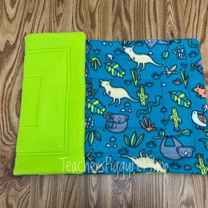 May include: A lime green fleece pad and a blue fleece blanket with an Australian animal print. The blanket features kangaroos, koalas, sloths, and cacti. The text "Teachers Piggy Pet Shop" is visible on the blanket.