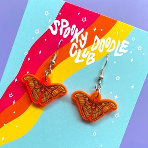May include: Orange and brown butterfly earrings with silver hooks. The earrings are on a card with the text "Spooky Doodle Club" and "By Elaina Smith Spookydoodleclub.etsy.com".