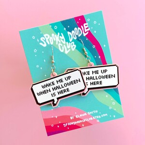 May include: Pink and white pixelated speech bubble earrings with the text "Wake me up when Halloween is here". The earrings are on a card with the text "Spooky Doodle Club" and "By Elaina Smith Spookydoodleclub.etsy.com".