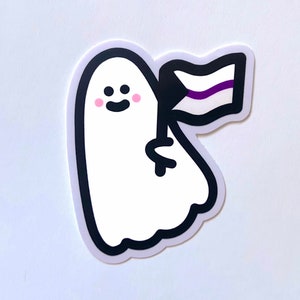 Op de afbeelding: Een witte geest met een zwarte omtrek en roze wangen houdt een zwart, wit en paarse vlag vast. De vlag heeft een zwarte streep bovenaan, een witte streep in het midden en een paarse streep onderaan.