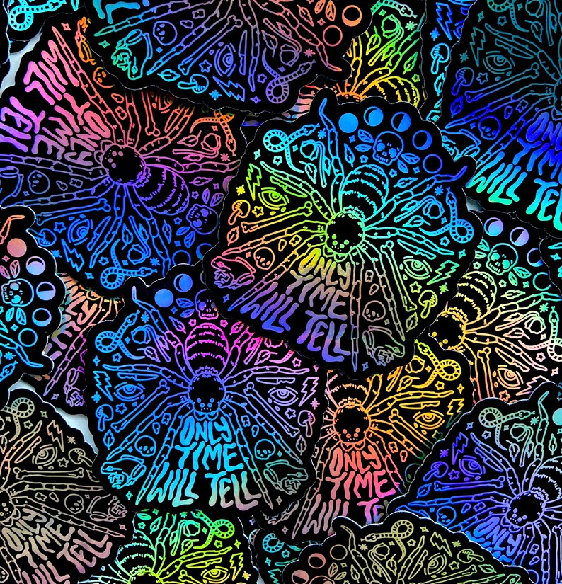 May include: A collection of iridescent holographic stickers featuring a spider with the text "Only Time Will Tell". The stickers are black with rainbow holographic accents and feature a variety of other designs, including eyes, moons, and snakes.