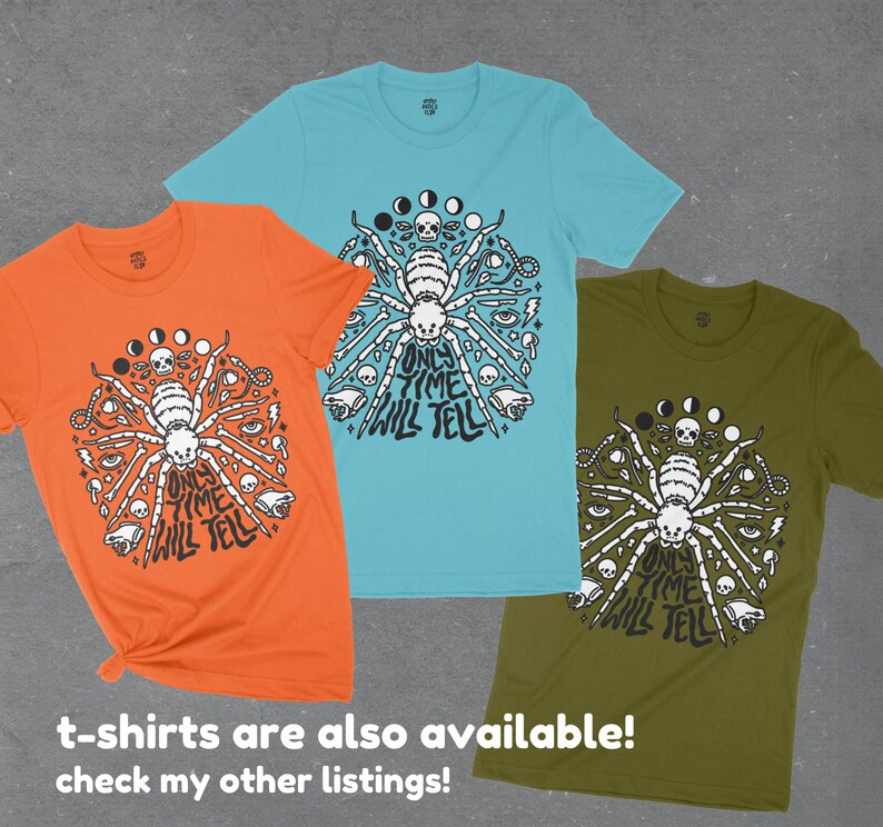 May include: Three t-shirts with a black and white graphic of a spider with the text "Only Time Will Tell" on a circle of moons, skulls, and eyes. The shirts are orange, turquoise, and olive green.