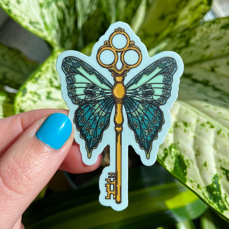 May include: A sticker featuring a gold key with a butterfly design. The butterfly wings are teal and green with a light blue background. The key has a decorative top with three circles.