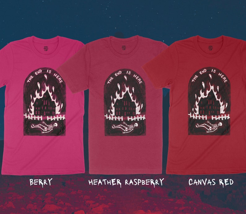 Op de afbeelding: Drie T-shirts met een grafische print van een brandend huis met een skelet dat er voor ligt. De tekst "The End is Here" is boven de print gedrukt. De T-shirts zijn in de kleuren bessen, heide-framboos en canvas rood.