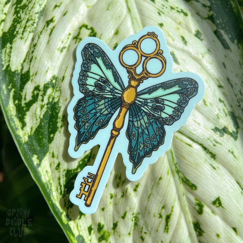 May include: A sticker featuring a gold key with a butterfly design. The butterfly wings are blue and green with a light blue background. The key has three holes in the top.
