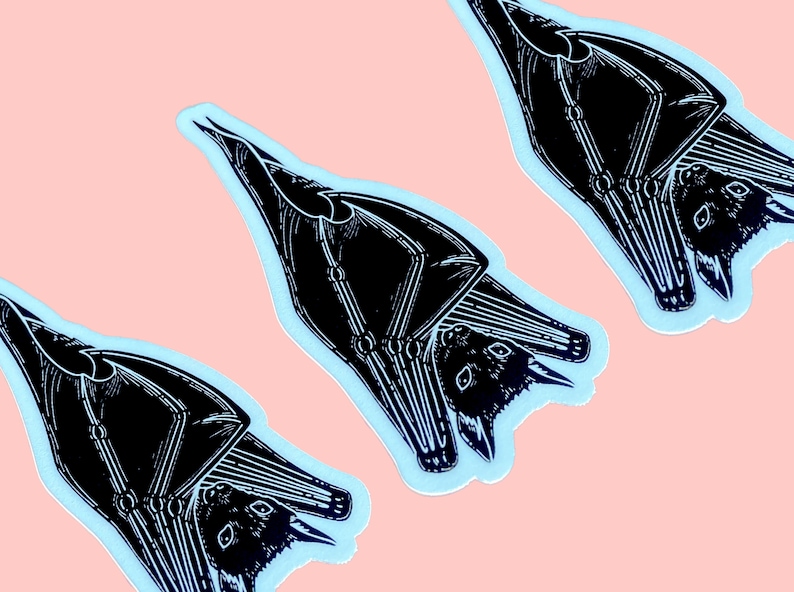 May include: Three black and white bat stickers on a light pink background. The bats are upside down with their wings spread out. The stickers are outlined in light blue.