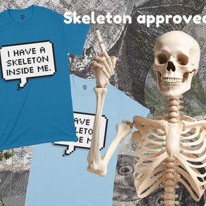 May include: A blue t-shirt with the text "I have a skeleton inside me." in a pixelated speech bubble. A skeleton with a friendly expression is giving a thumbs up. The text "Skeleton approved!" is above the skeleton.